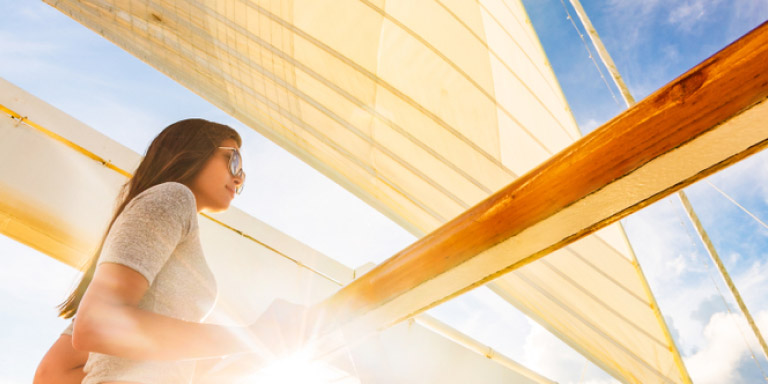 Young lady wearing sunglasses leaning against a rail on a yacht.